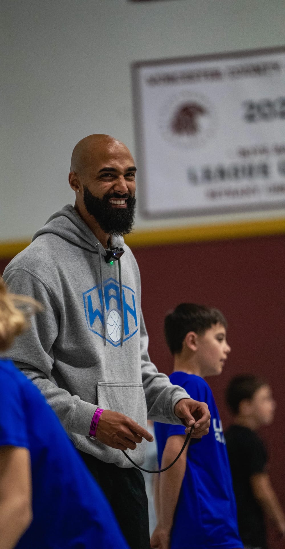 Coach Aaron Anniballi smiling courtside in a We All Hoop hoodie